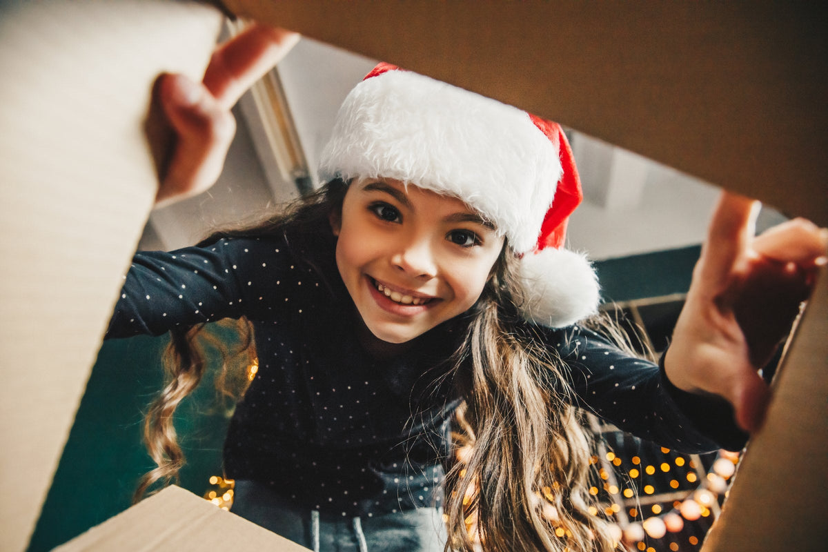 A delighted little girl opening a Christmas present by a decorated tree