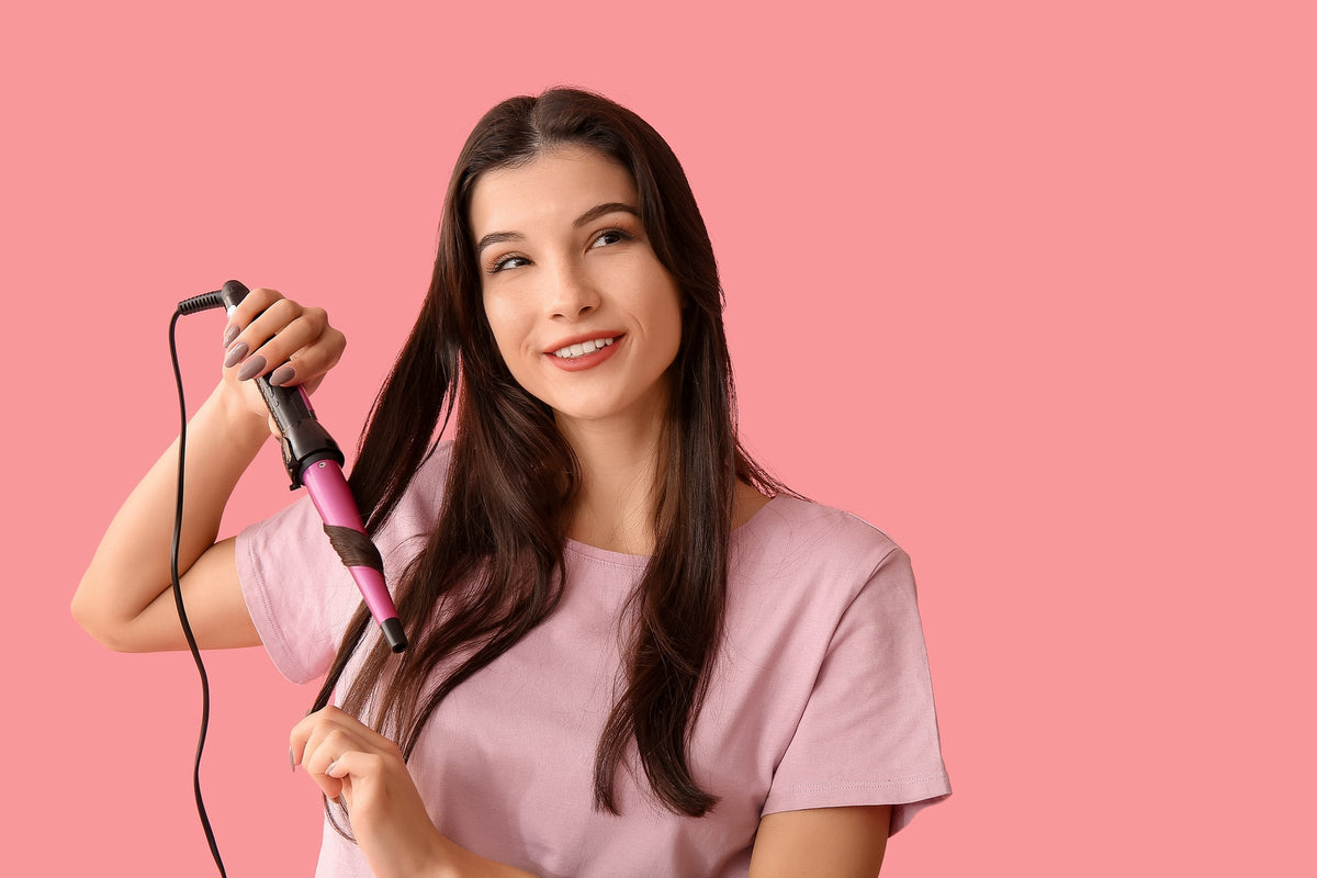 A woman curling her long dark hair with a curling iron