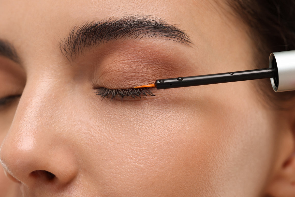 A woman applying serum to her eyelashes, close up
