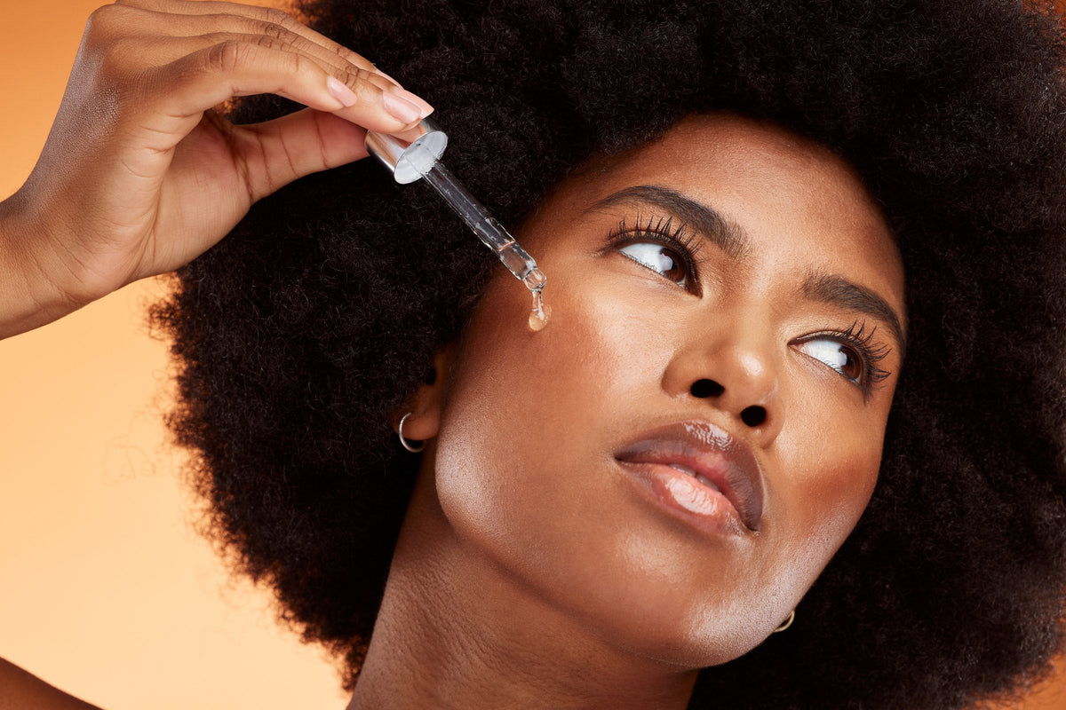 A woman holding a dropper of face serum to her cheek