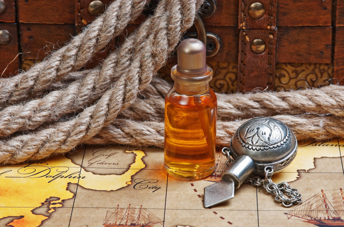 A small glass vial of amber perfume oil beside a silver flask on an old map, with coiled rope behind