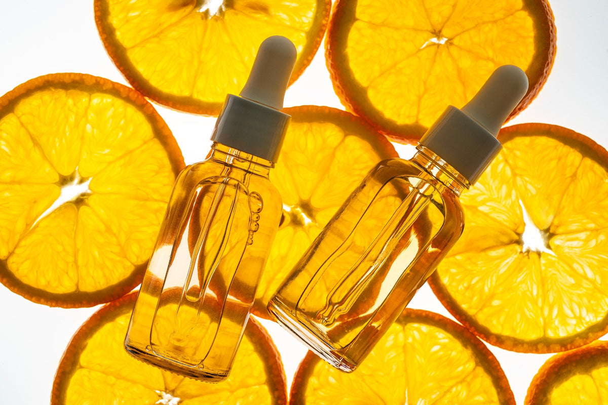 Vitamin C serum dropper bottles on backlit slices of orange