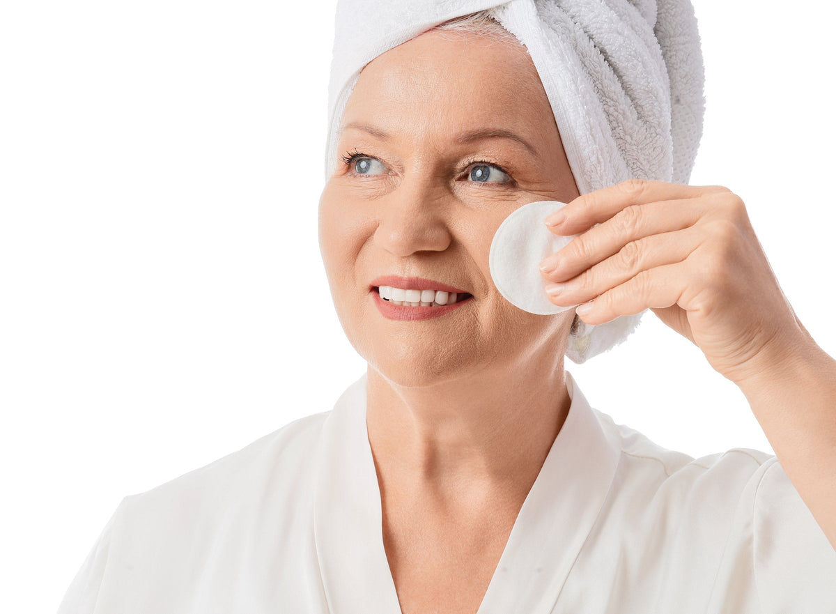 A woman in her fifties applying toner with a cotton pad to her face