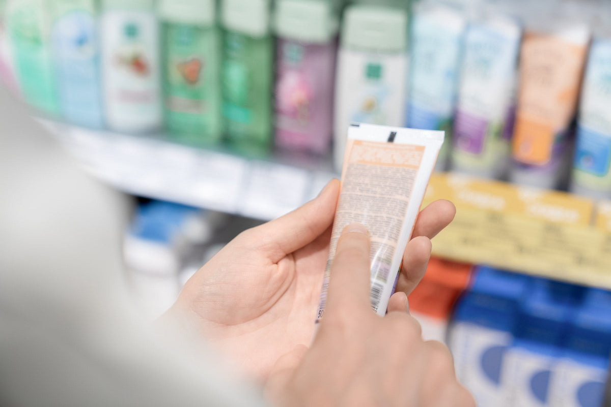A woman reading the ingredients on a tube of skin cream in a shop