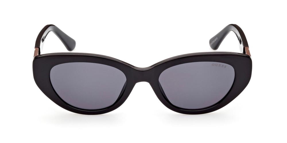 Black cat-eye sunglasses with gold logo accents on temples and dark tinted lenses on white background