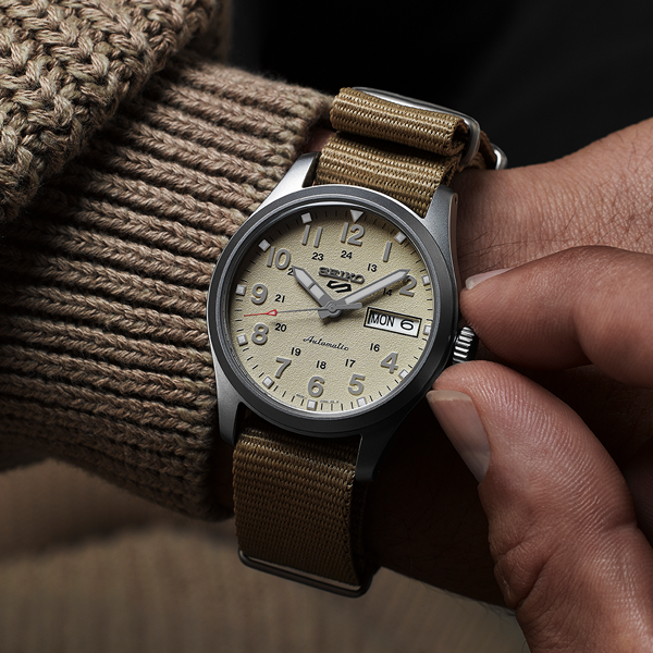 Beige dial field watch with fabric strap, silver case, brown accents, day-date window